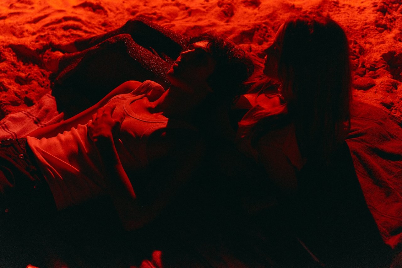 Couple lying close together on sand, bathed in deep red light at night