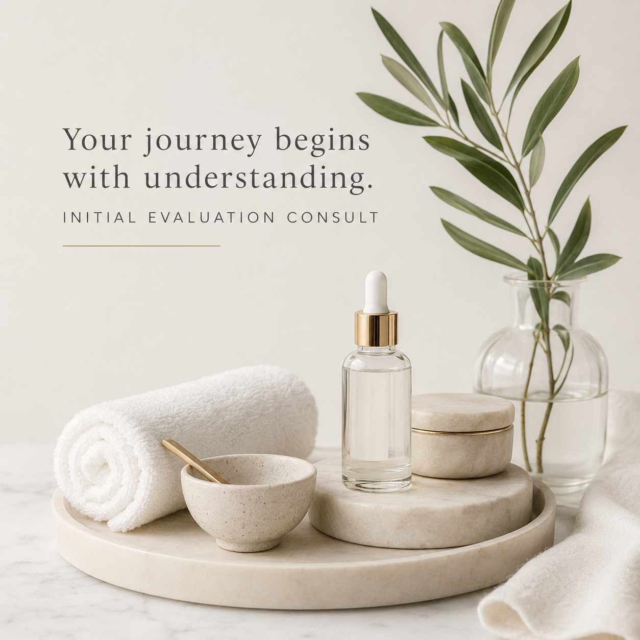 Minimalist spa or skincare setting with a rolled white towel, a small bowl with a gold spoon, a glass dropper bottle of serum, stacked marble containers, and a glass vase with green leafy branches, with text reading 'Your journey begins with understanding. Initial evaluation consult.'