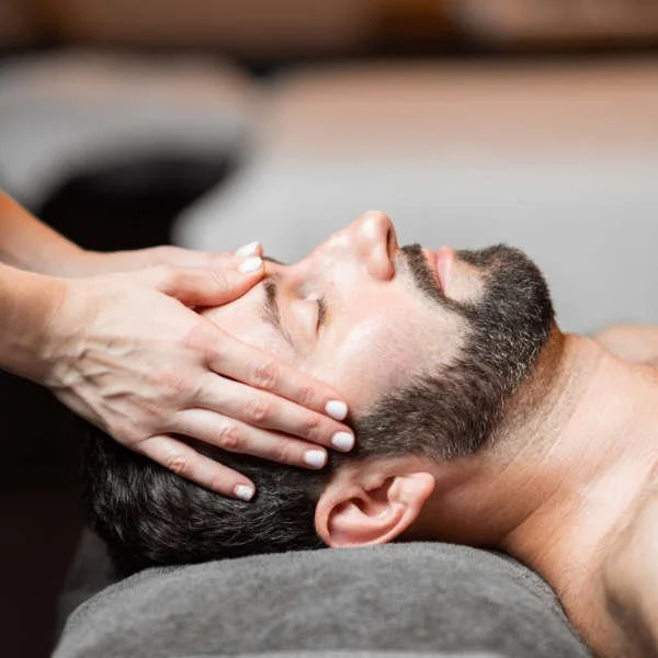 Person receiving a facial massage or skincare treatment with hands on their face, lying down with closed eyes.