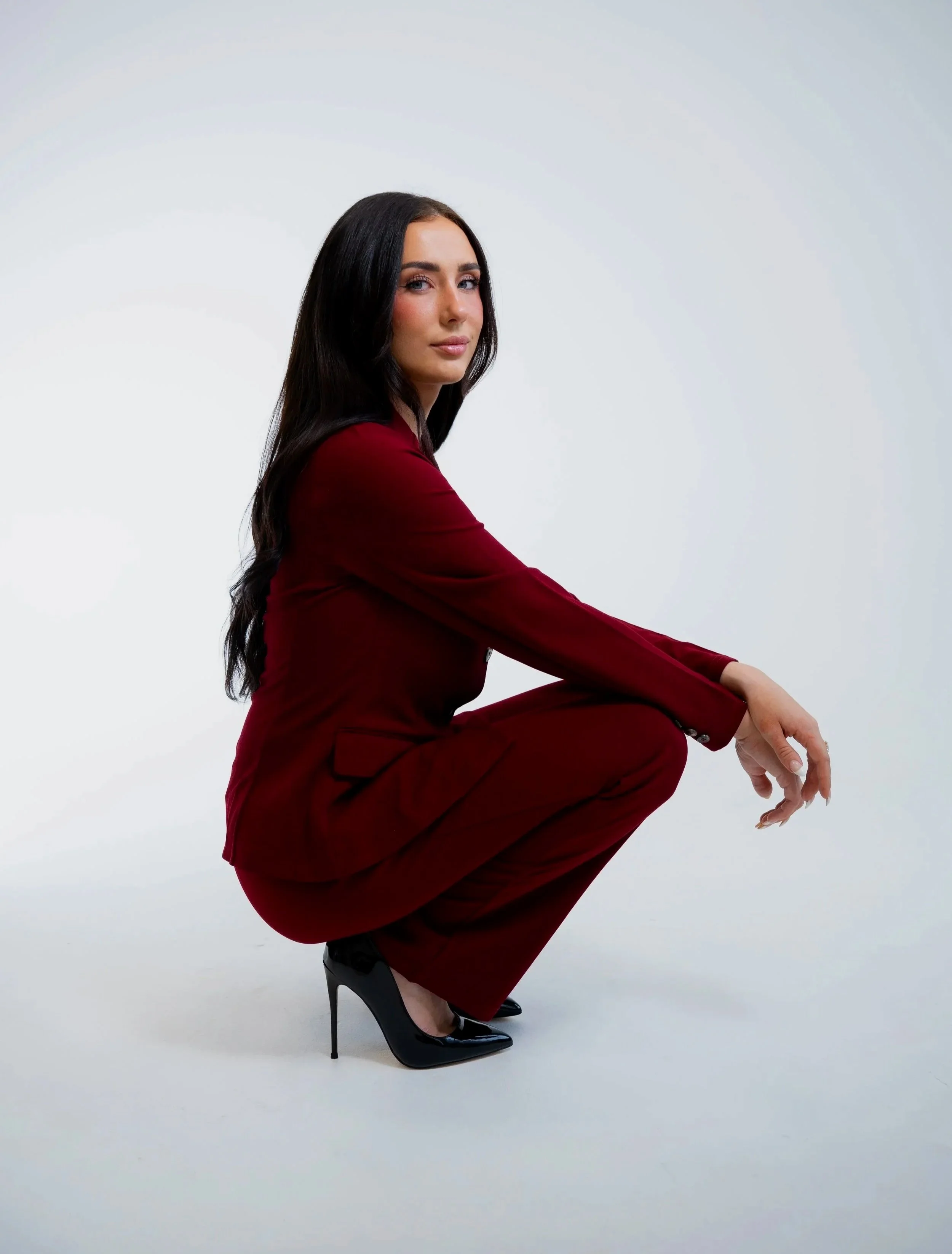 A UGC creator with long dark hair, wearing a red suit and black high heels, posed against a plain light background.