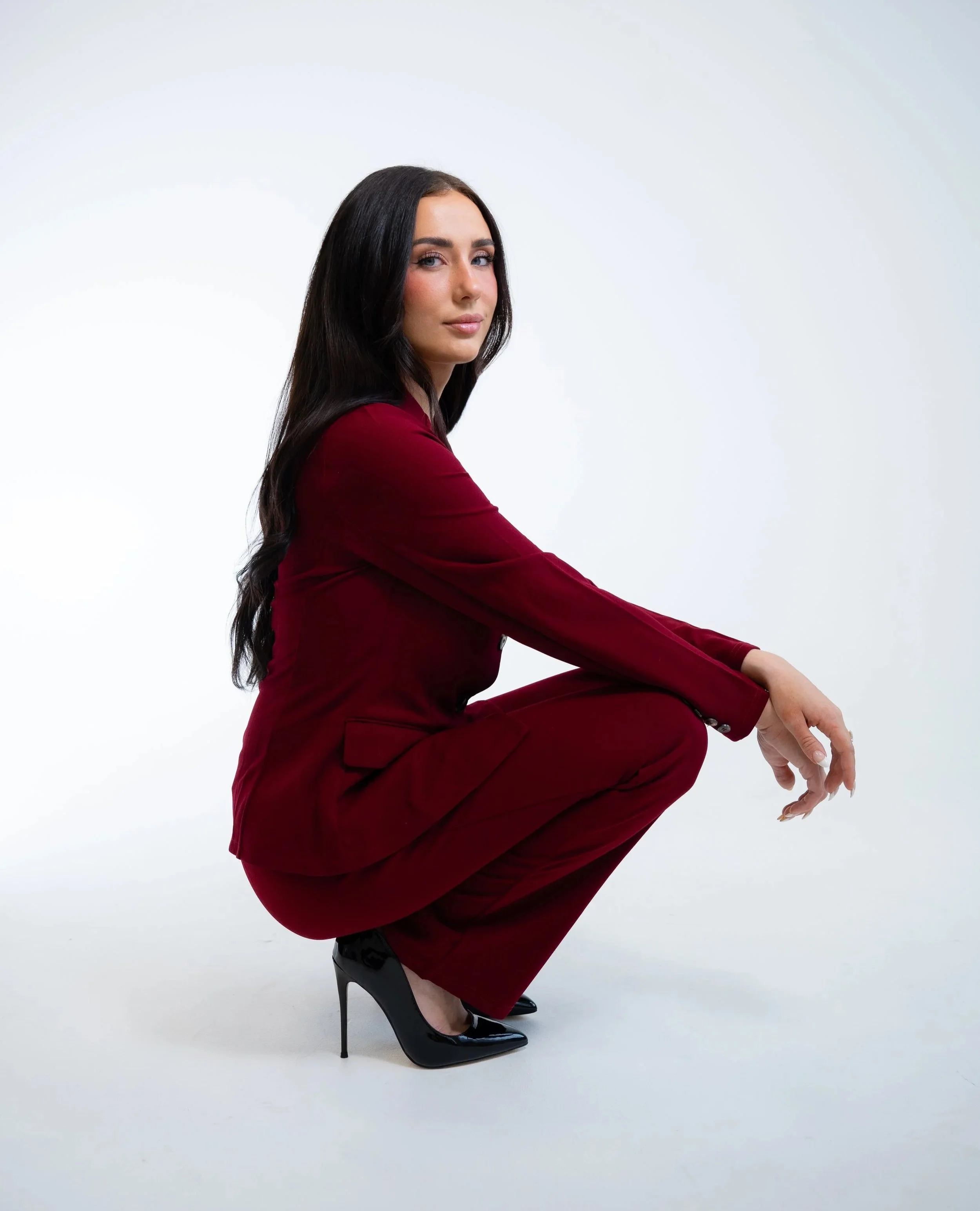 UGC creator in a red outfit and black high heels squatting against a plain white background