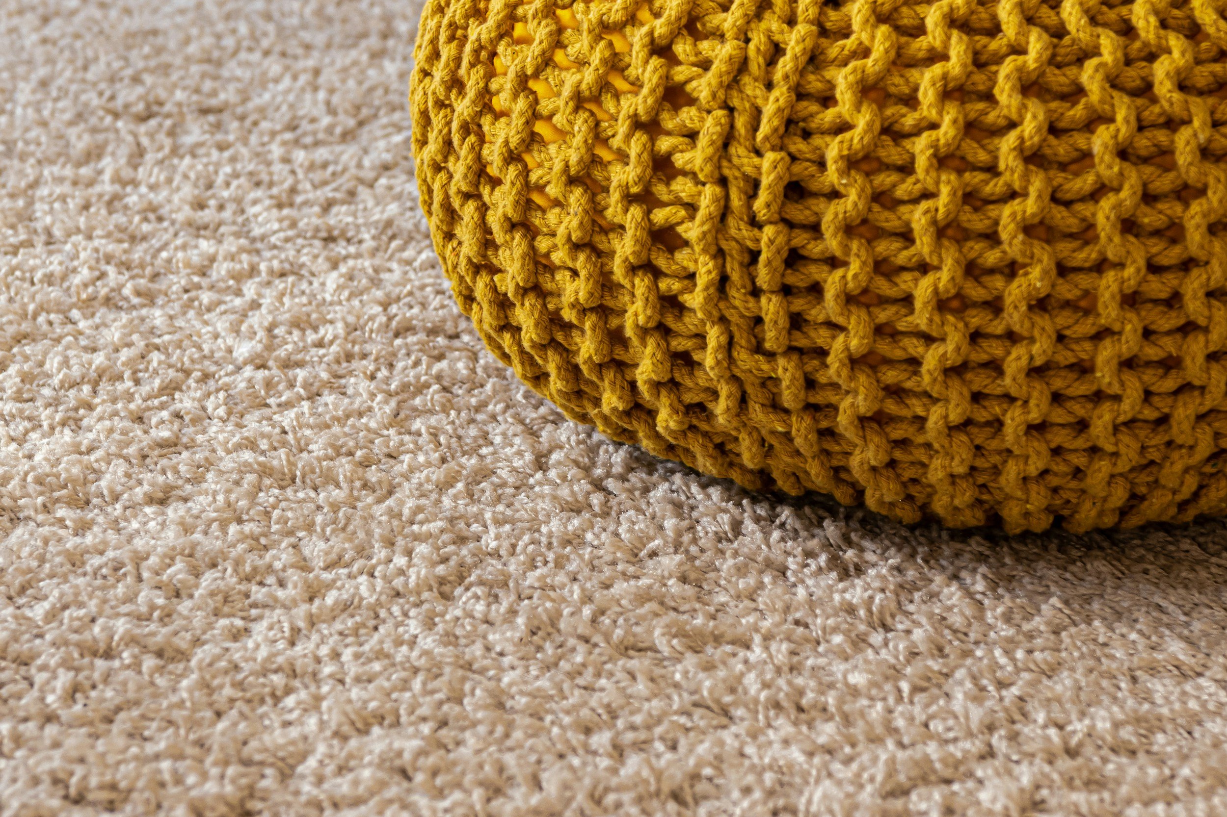 Close-up of a yellow, knit, decorative object on a beige carpet.