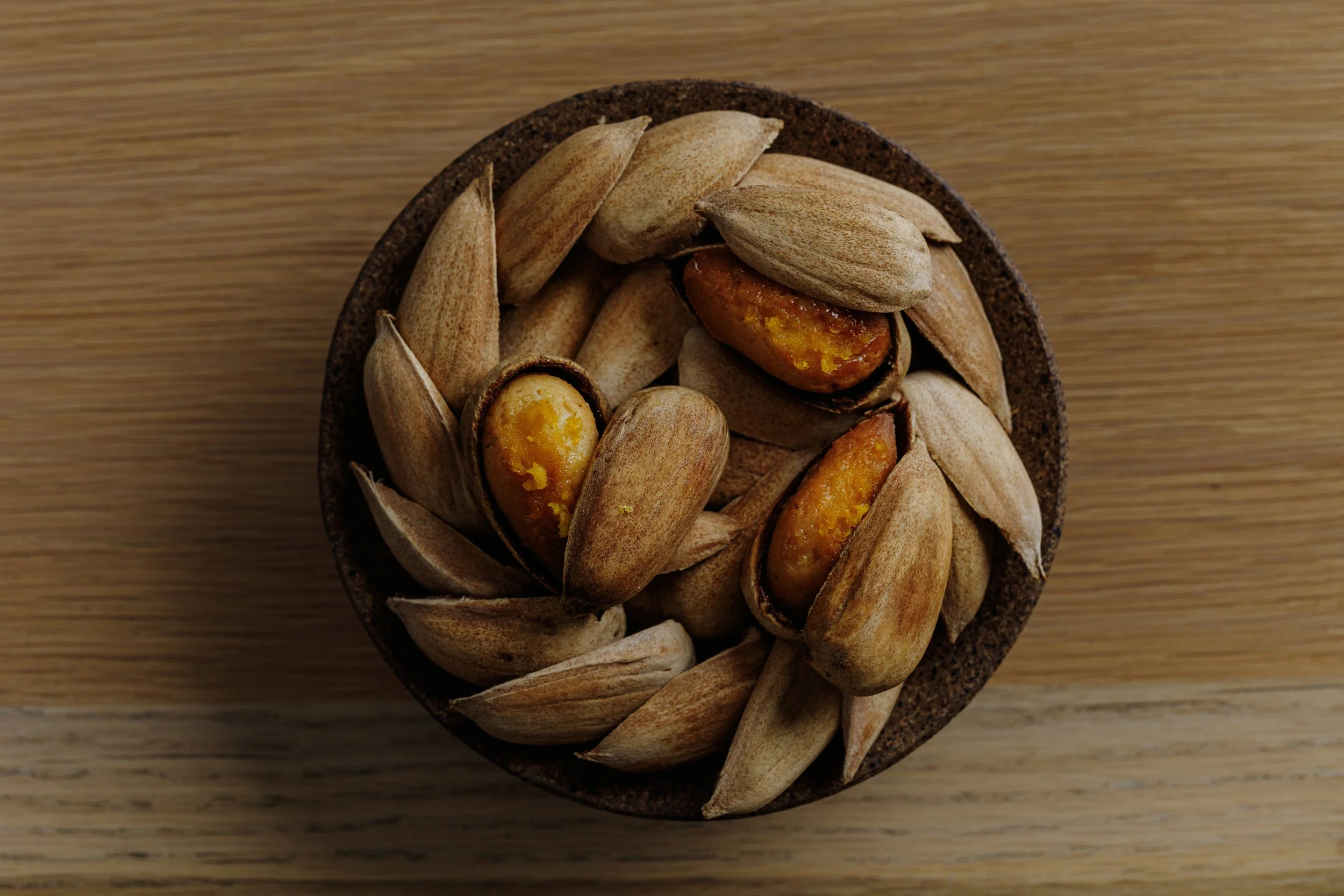 A top-down view of a small bowl filled with roasted pistachio nuts on a wooden surface.