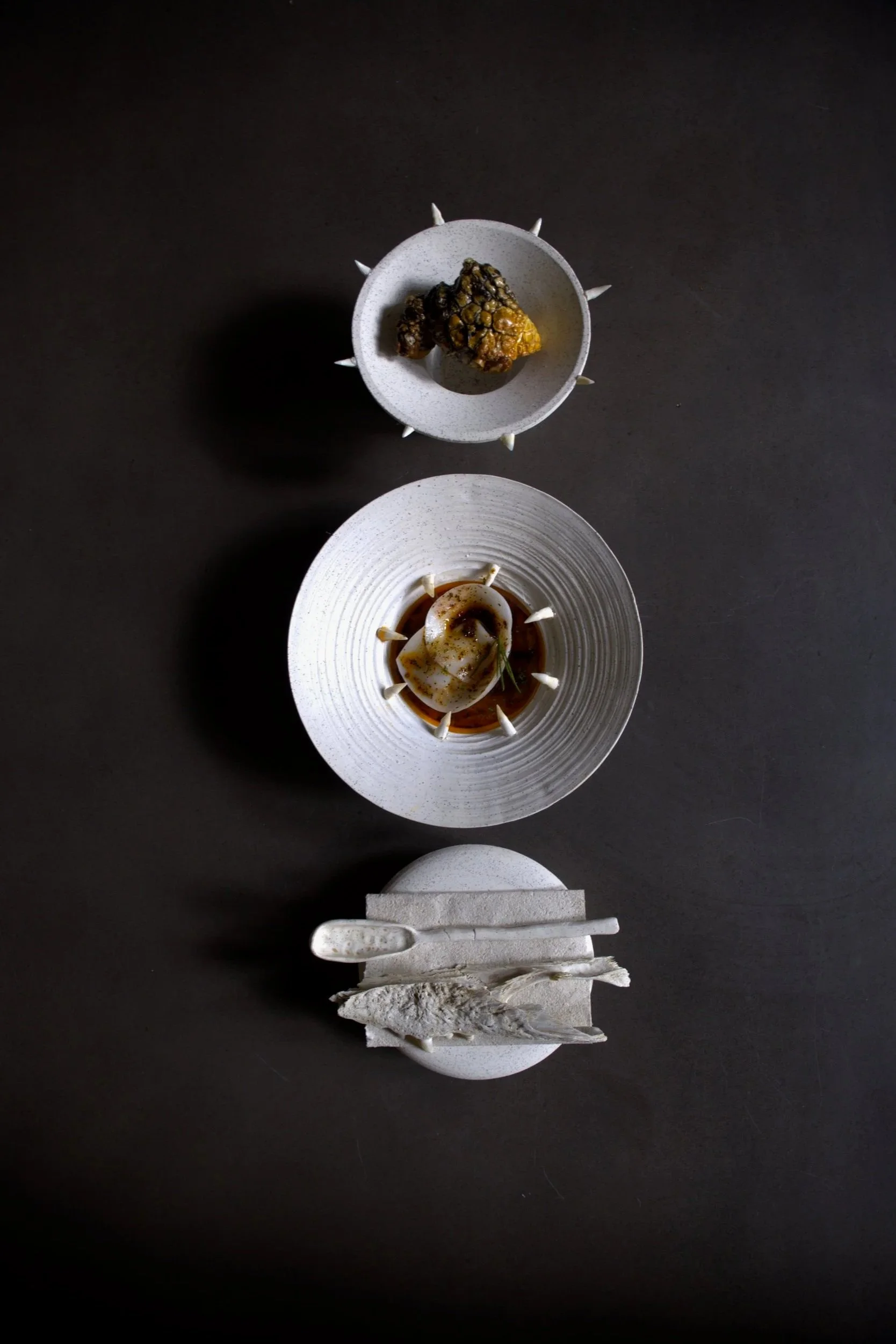 Top view of three dishes on black background with chopsticks, featuring gourmet food and decorative elements.