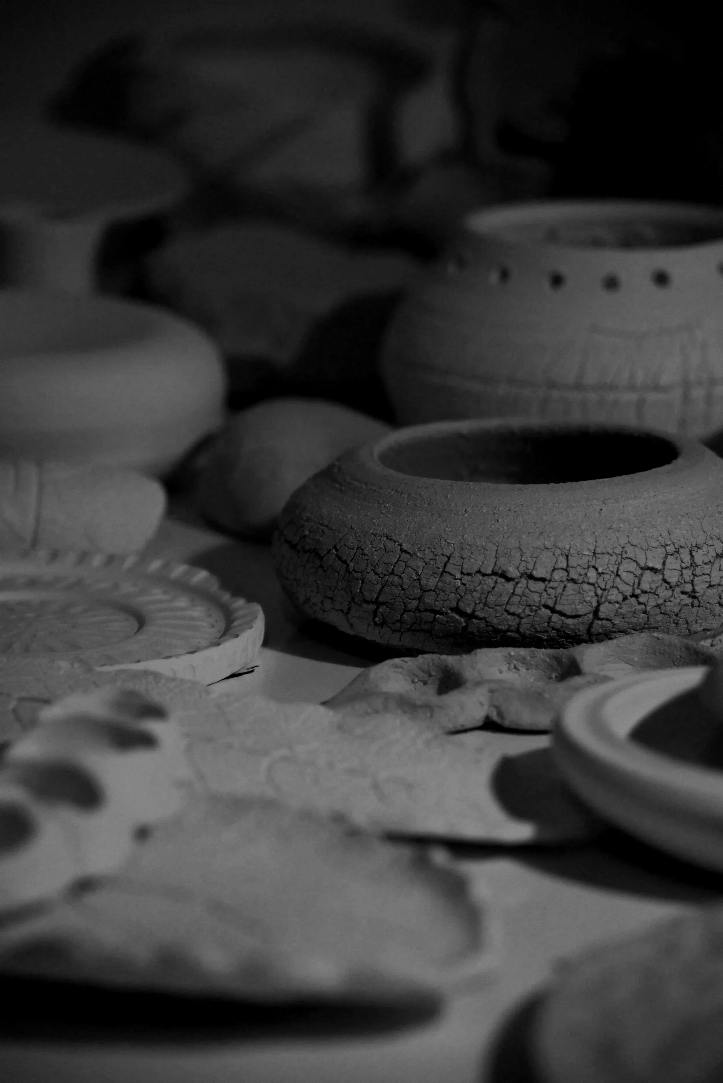Close-up of pottery or ceramic objects with cracked and textured surfaces, some with holes or pattern details, in black and white.