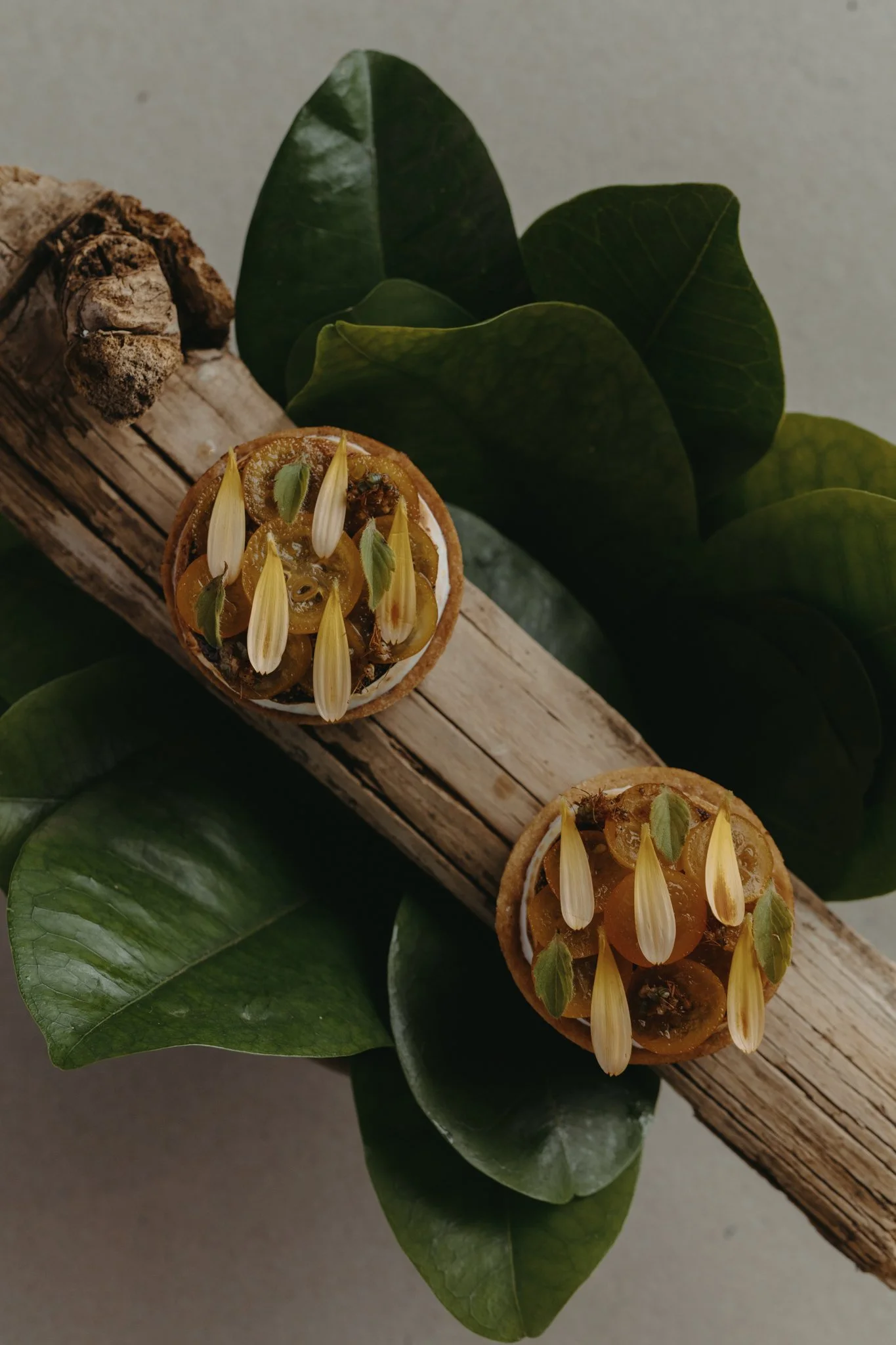 Close-up of a wooden stick with green leaves and a decorative object made of small yellow and green elements on top of it, set against a neutral background.