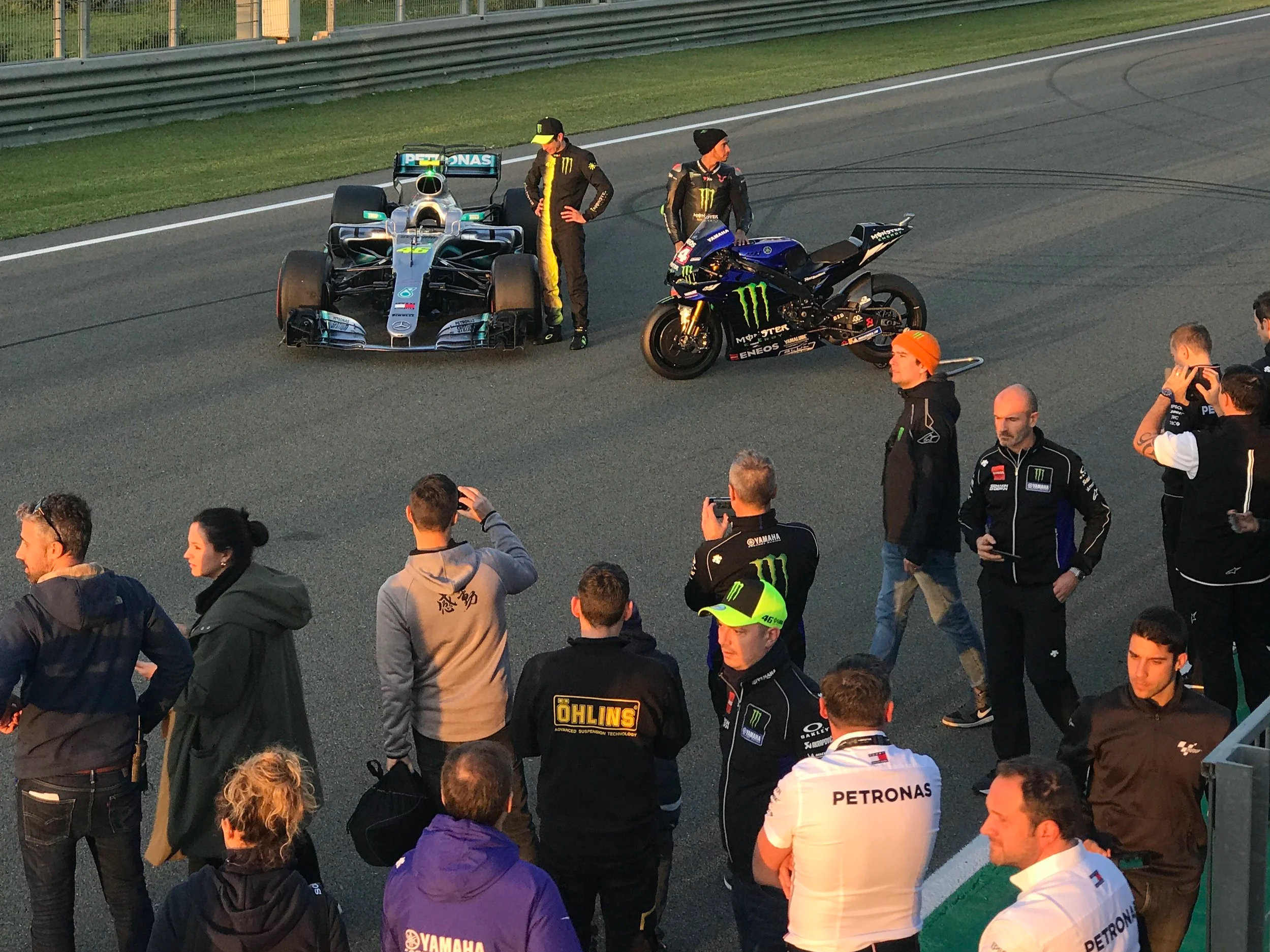 Formula 1 race car in a parking lot with two team members and several spectators around.
