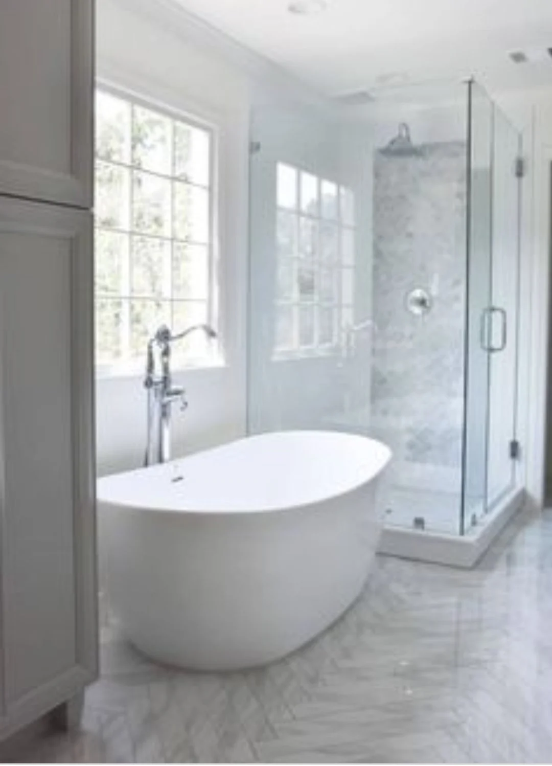 Modern bathroom with a freestanding bathtub, large window, and glass-enclosed shower with marble tiles.