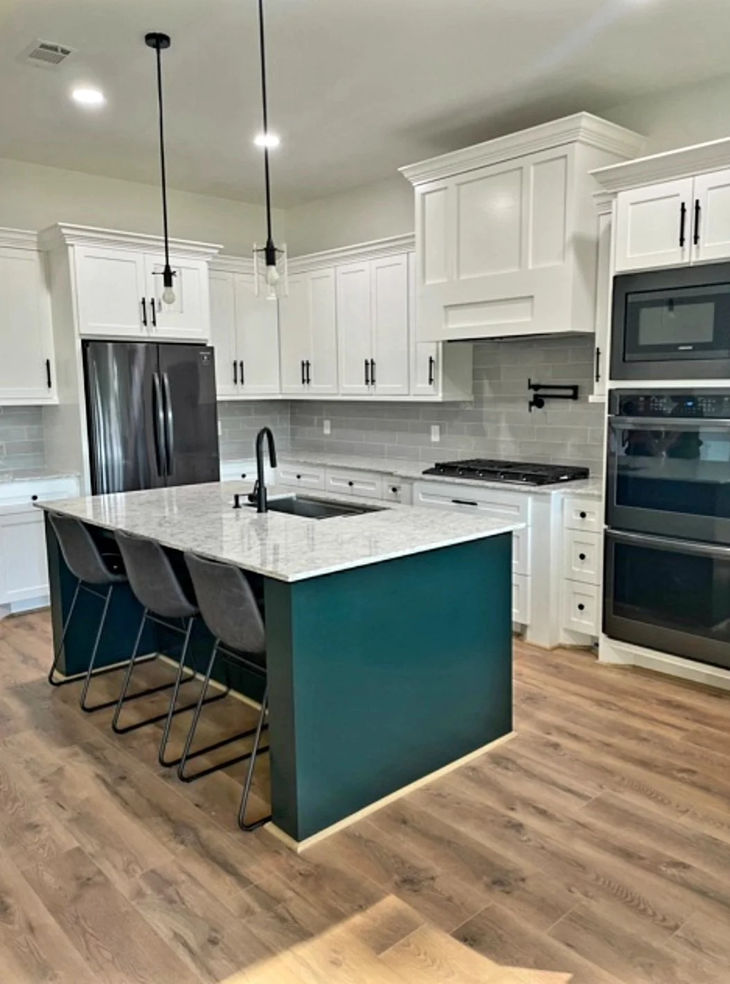 Modern kitchen with white cabinets, stainless steel appliances, gray backsplash, green island with marble countertop, three gray chairs, and wood flooring.