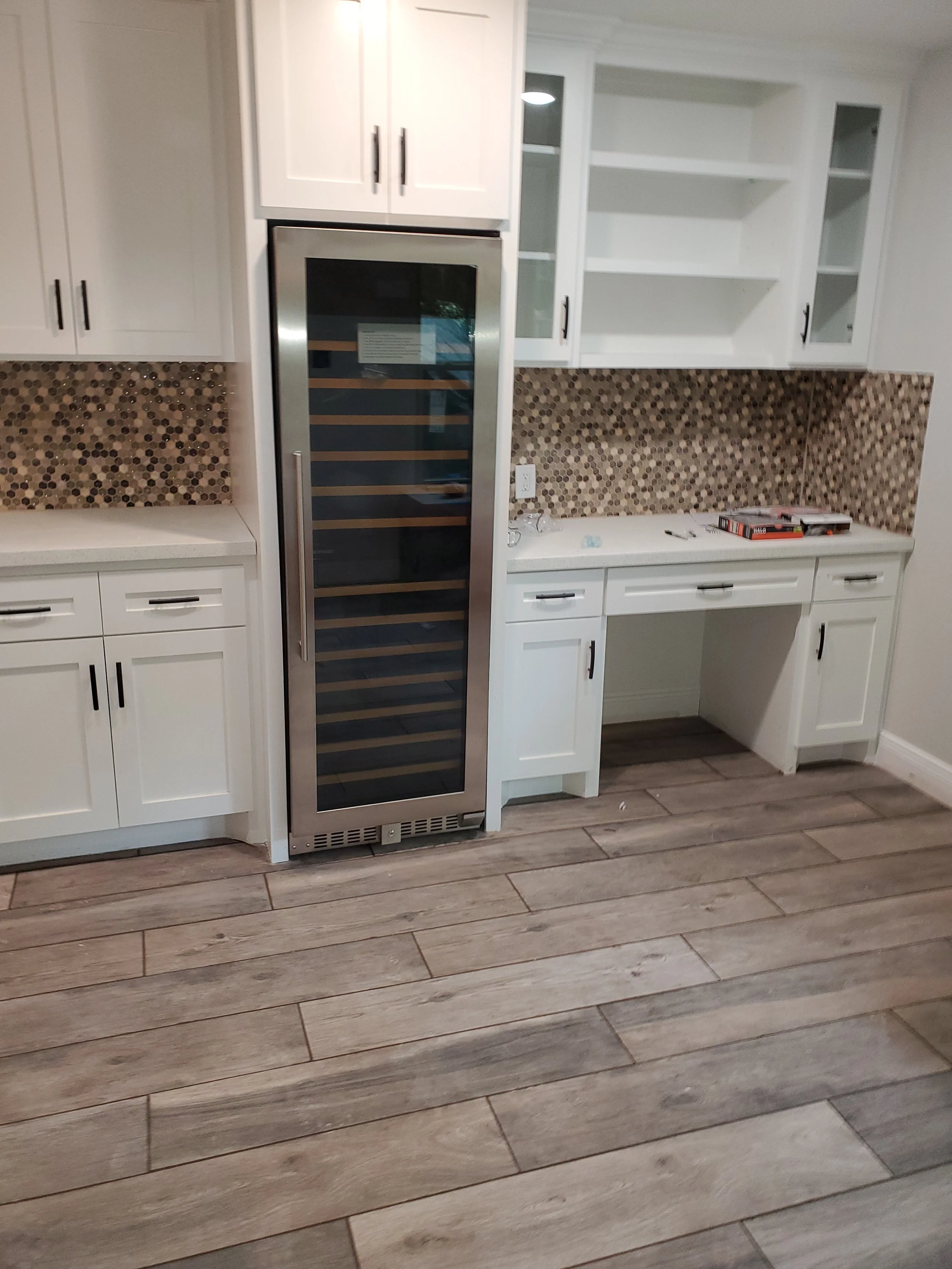 Kitchen with white cabinets, a built-in wine cooler, and a mosaic tile backsplash with a countertop. There are some tools and a box on the counter.