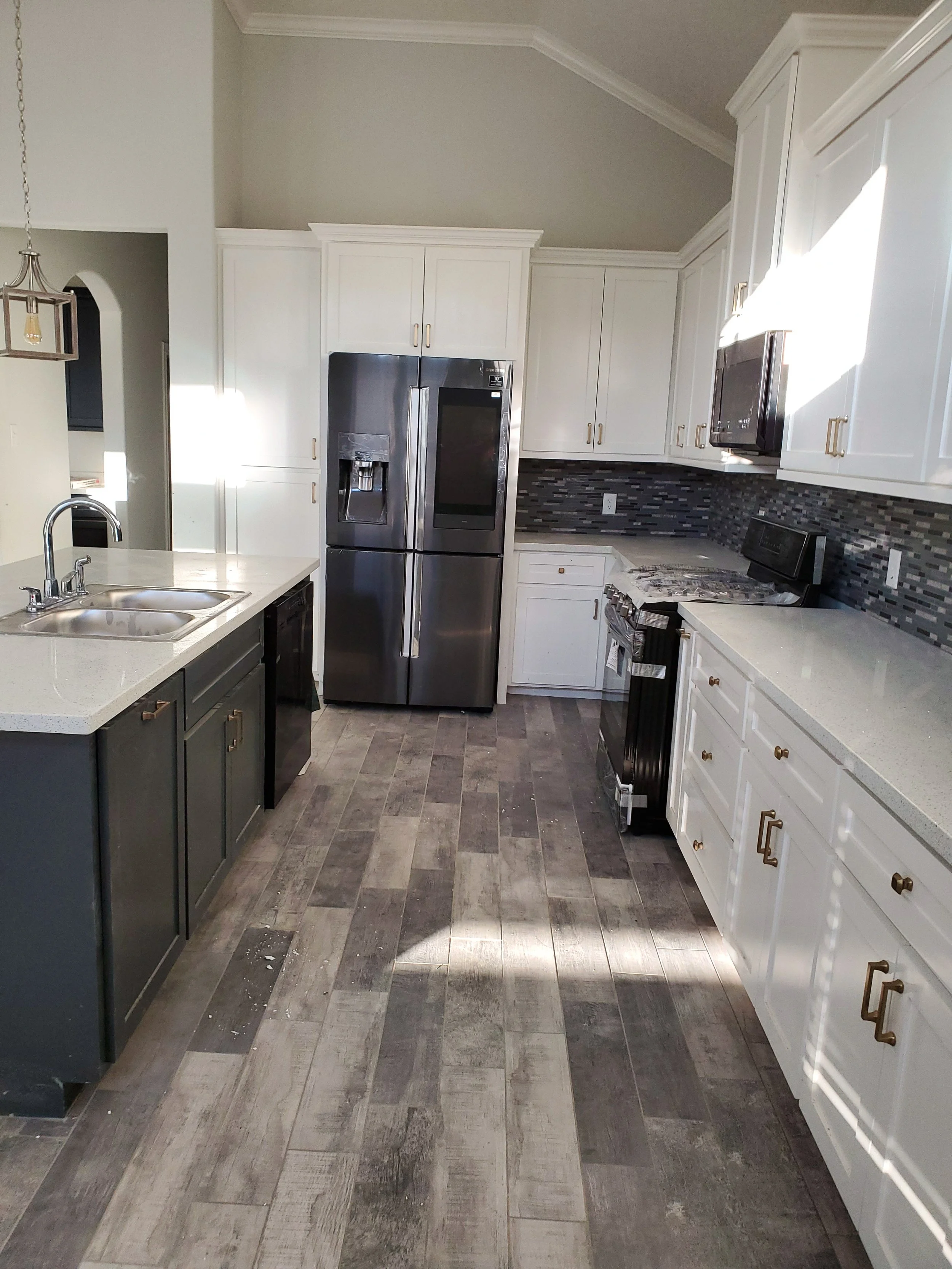Kitchen with white and dark gray cabinets, stainless steel refrigerator, black stove, gray and brown tile flooring, and a black backsplash with gray accents.