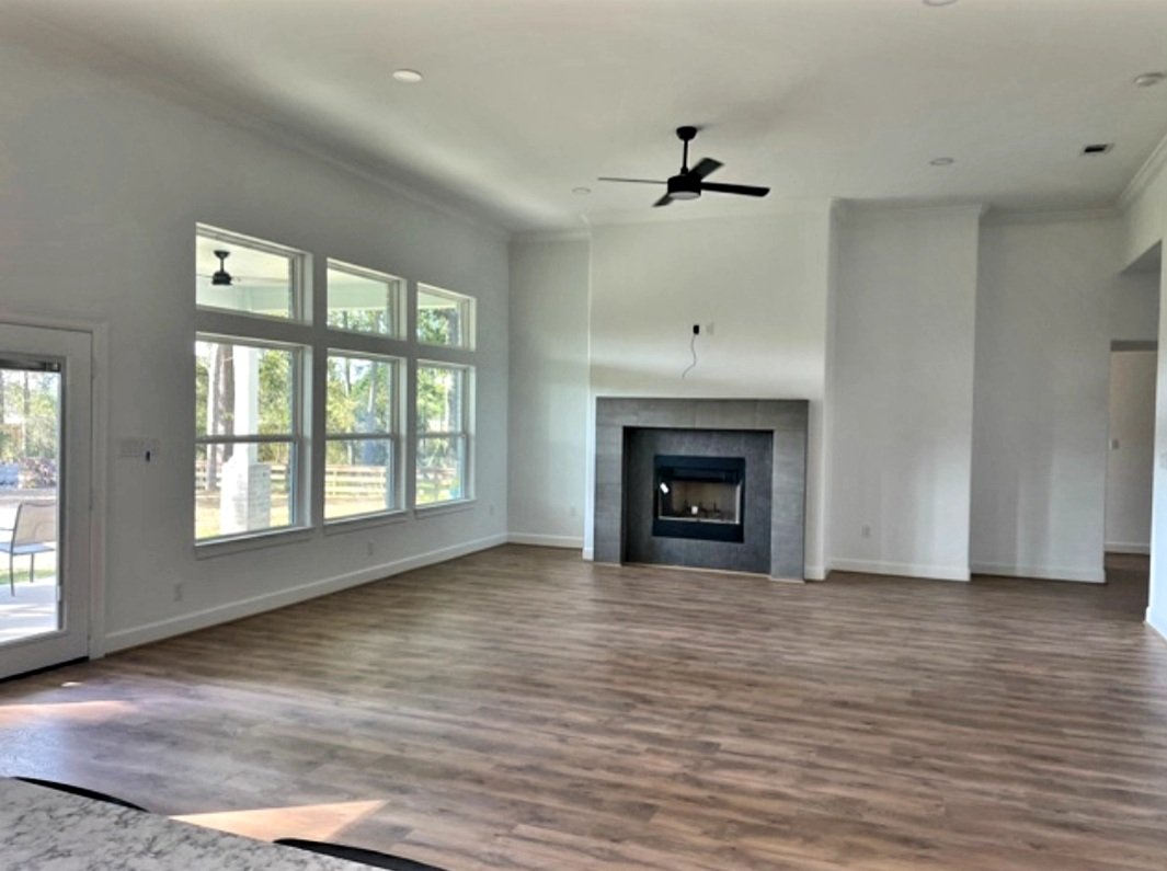 Empty living room with large windows, a fireplace, and wood flooring.