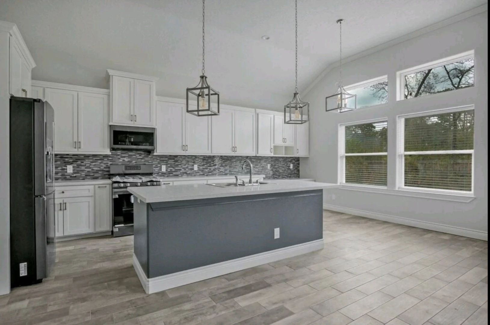 Modern kitchen with white cabinets, gray island, mosaic tile backsplash, large windows, and pendant lighting.