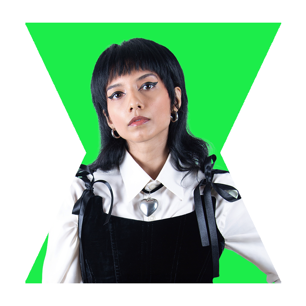 A woman with black hair wearing a white shirt, black velvet dress with ribbon shoulder ties, and a heart-shaped pendant.