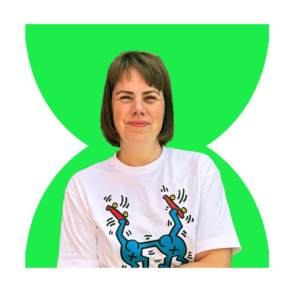 A woman with short brown hair smiling, wearing a white T-shirt with a colorful abstract design.
