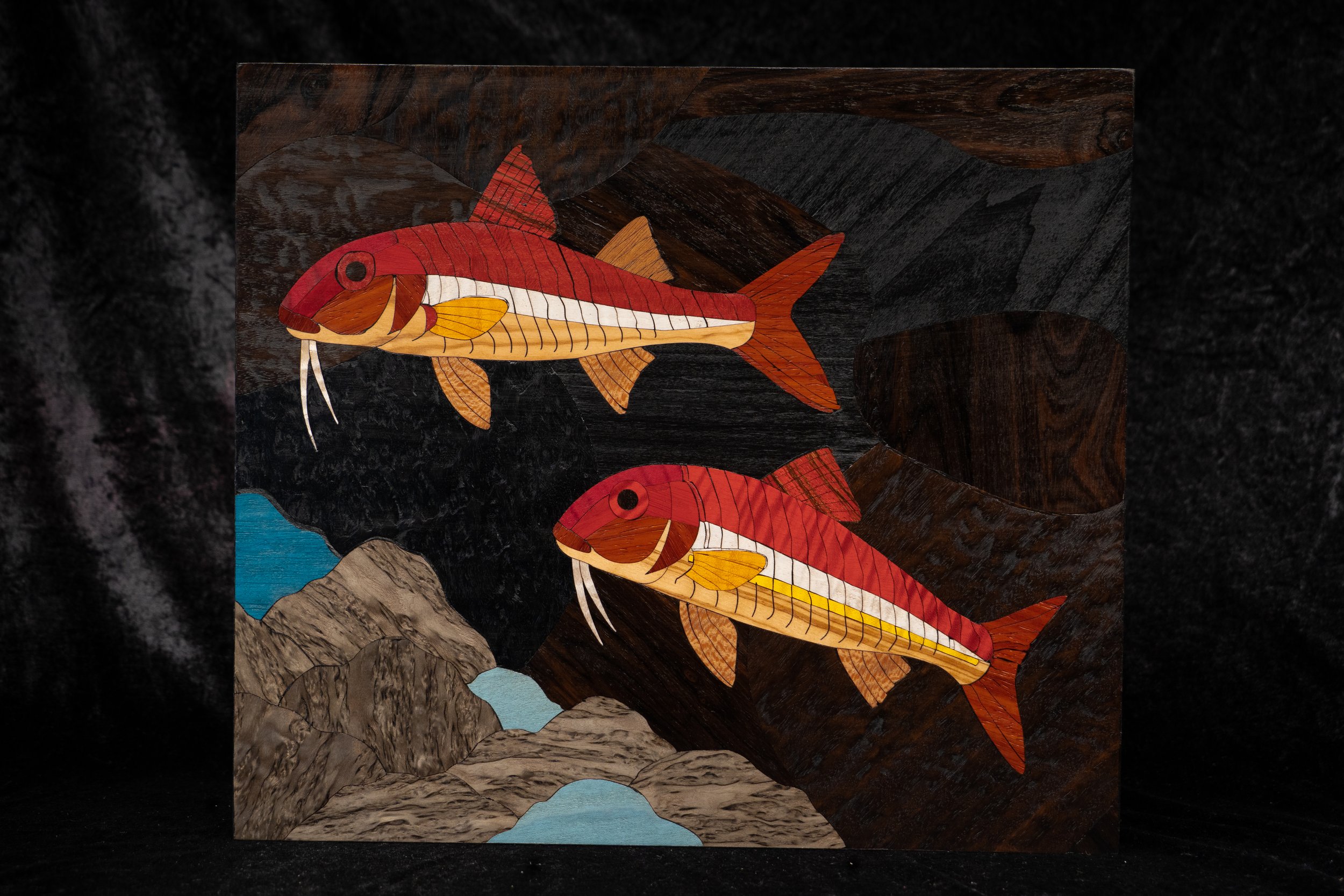 Une œuvre d'art représentant des poissons rouges en bois sculpté, avec un paysage rocheux et une montagne en arrière-plan.