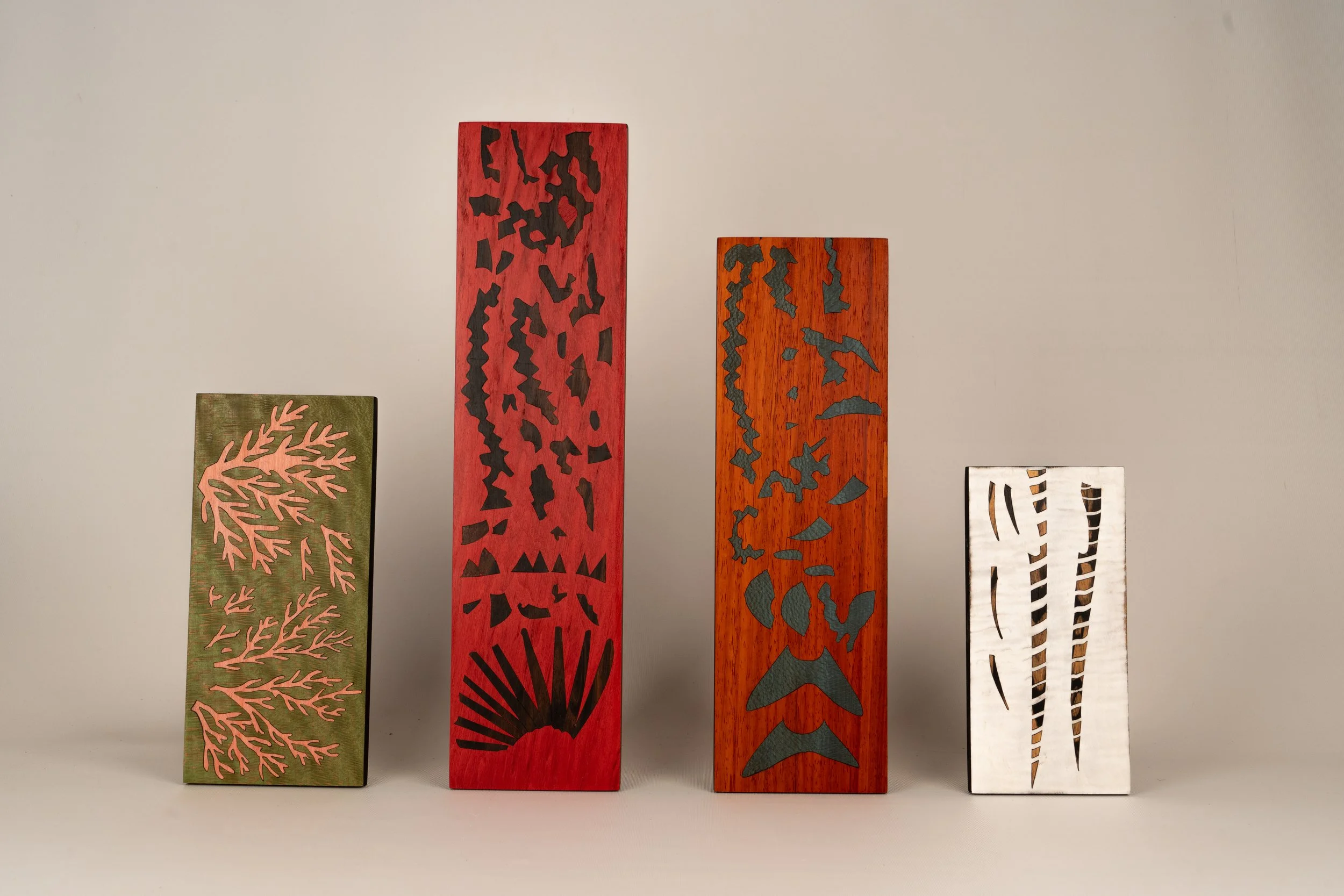 Quatre planches en bois peintes avec des motifs abstraits, alignées verticalement contre un mur neutre.