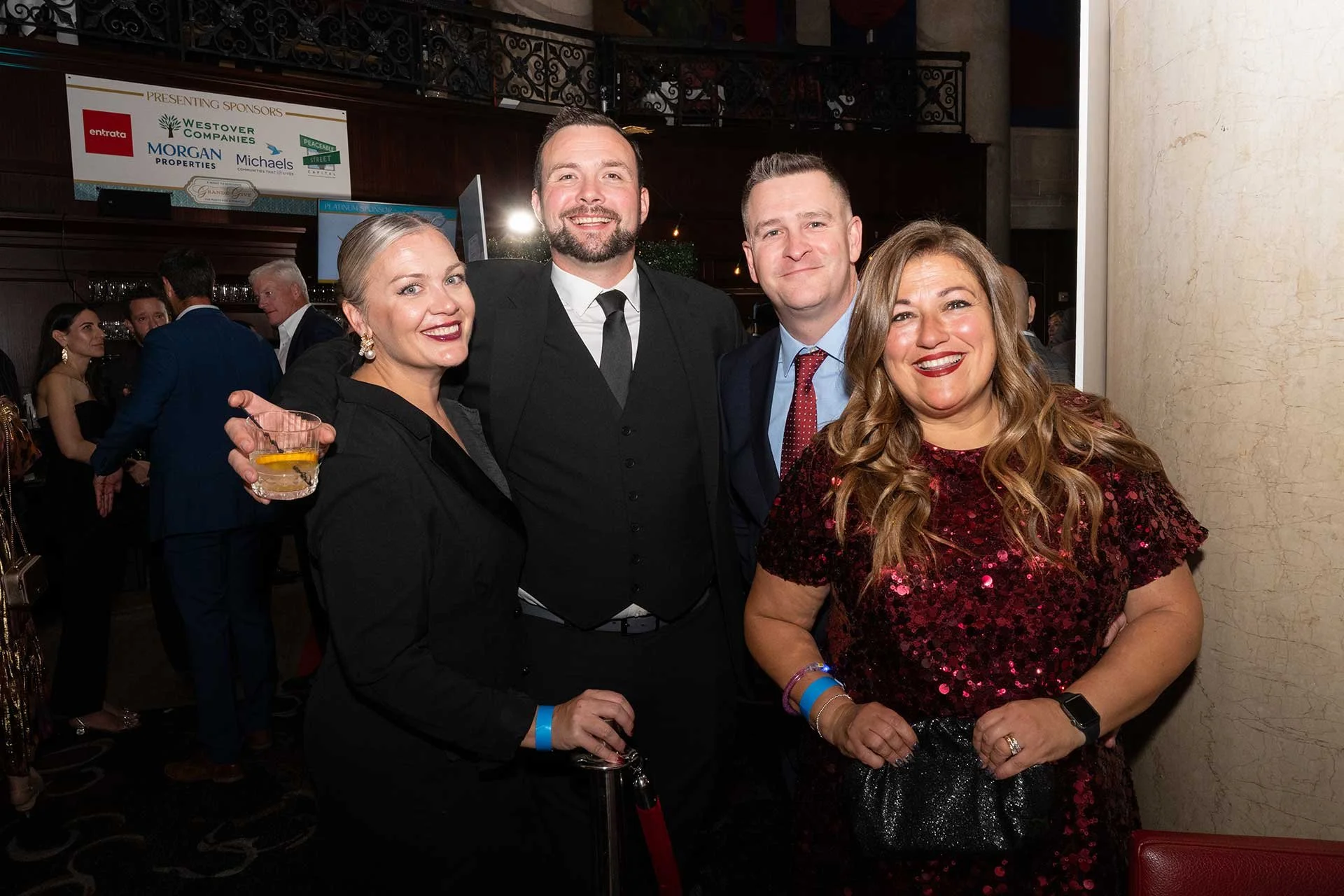 two couples at a fundraiser dressed in fancy clothes and smiling at the camera for a photo