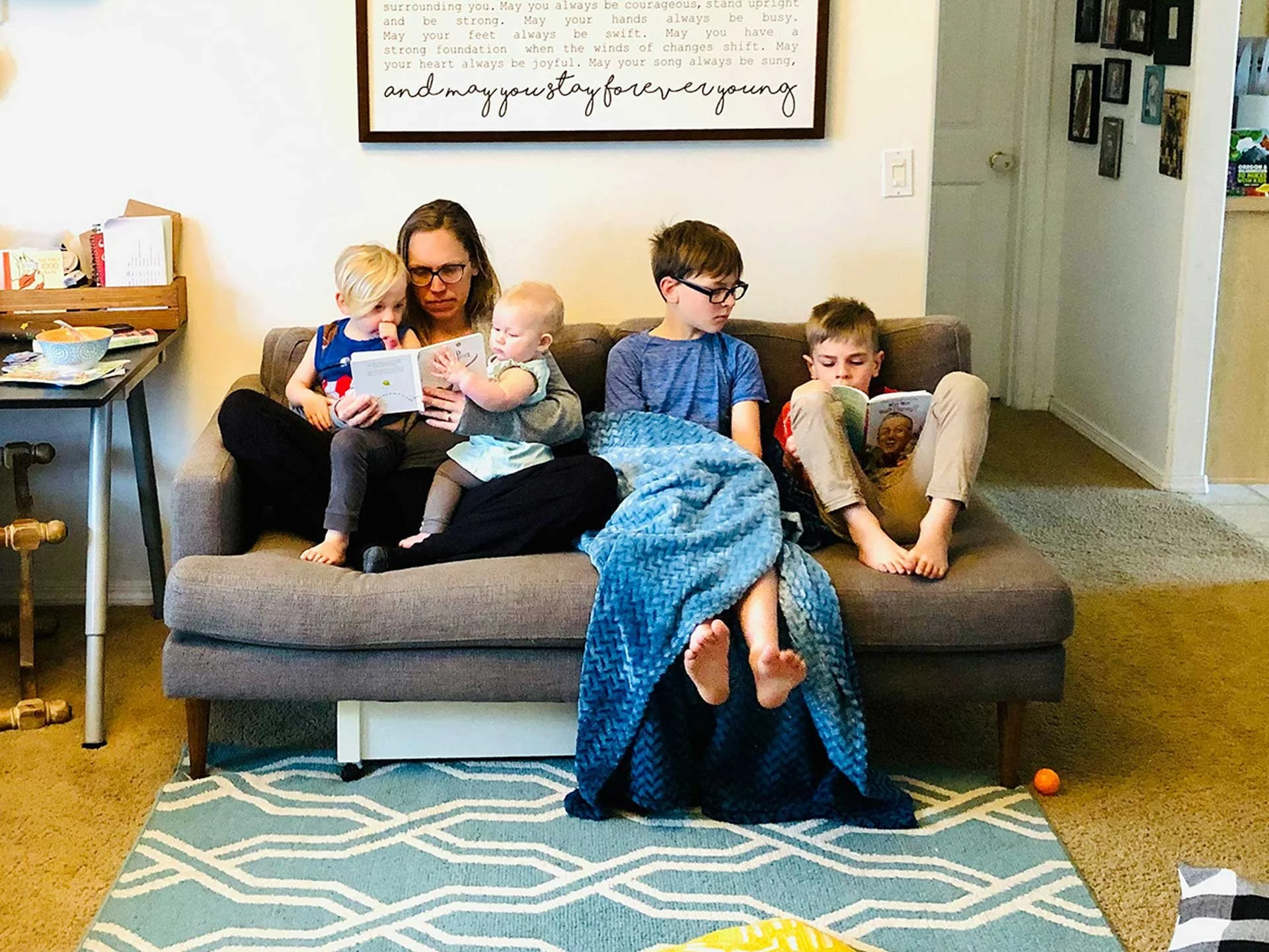 Mom sitting on a couch reading with four kids gathered together on a cozy couch in their living room