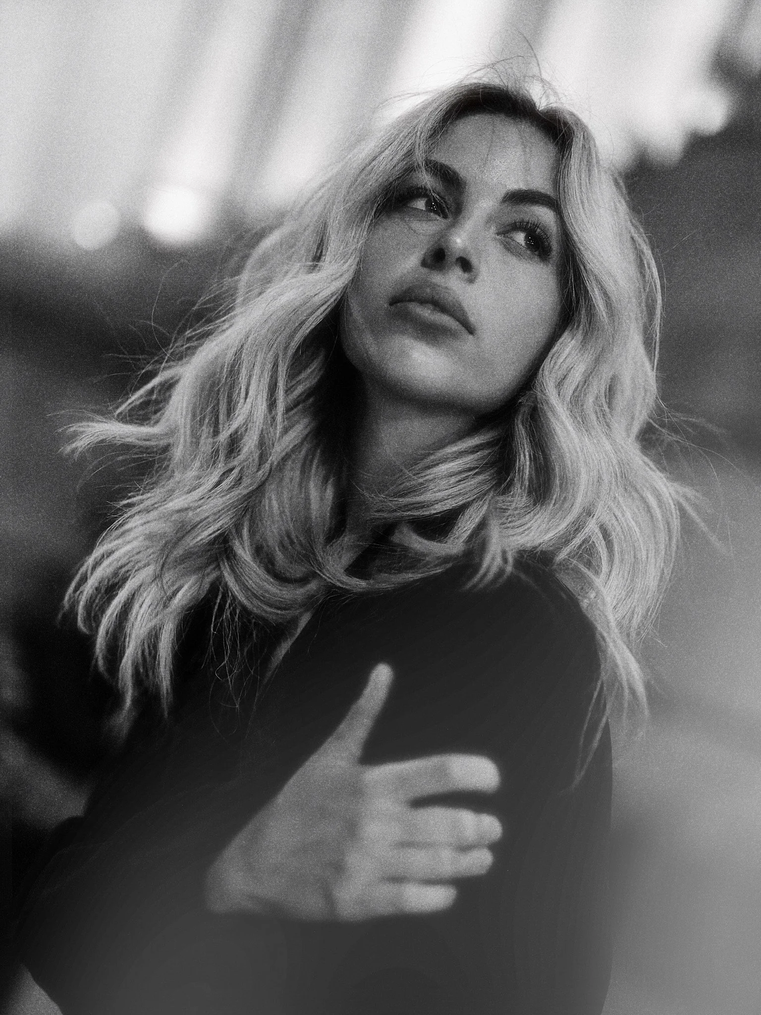 A black and white photograph of a woman with long, wavy hair, and a serious expression on her face. She is holding her hand close to the camera, with fingers slightly spread.