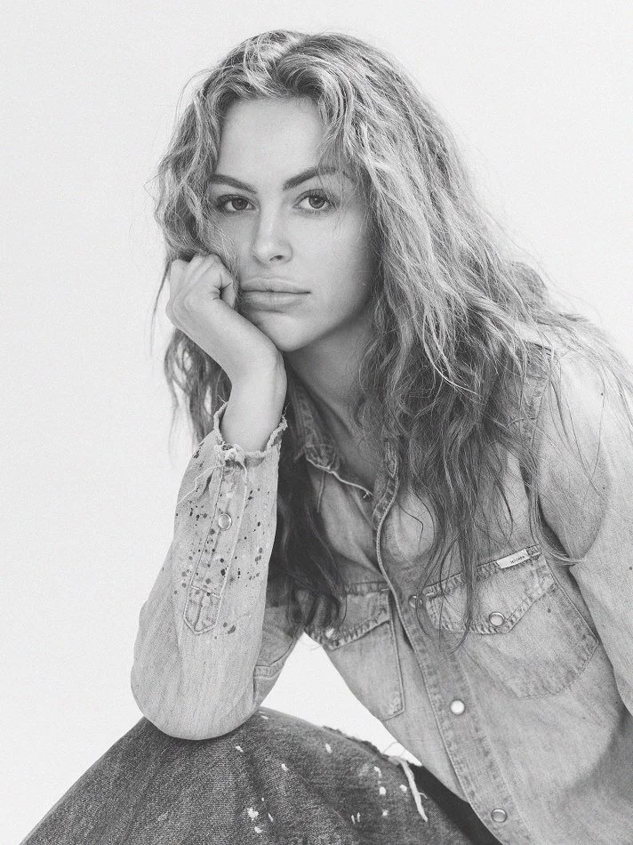 Black and white portrait of Noémi, a young Montréal female model signed with MTL Models MGMT  with curly hair, wearing a denim jacket, modelling, resting her chin on her hand.