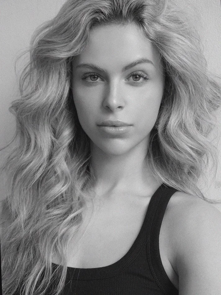 Black and white portrait of Noémi, a young Montréal female model signed with MTL Models MGMT  with long, wavy hair wearing a black tank top, looking directly at the camera modelling.