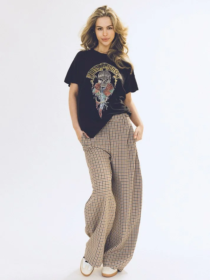 Noémi, a young Montréal female model signed with MTL Models MGMT wearing a black graphic band t-shirt and high-waisted plaid wide-leg pants, modelling against a plain white background.