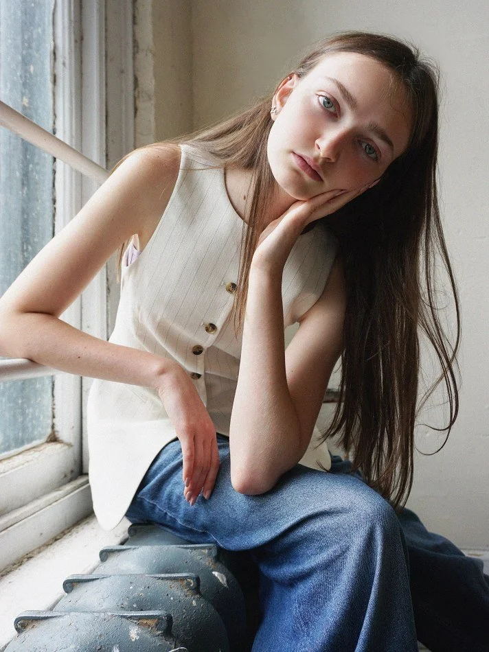 Sadie, a young Montréal female model signed with MTL Models MGMT modelling agency. She has long brown hair and fair skin sitting on a window sill, resting her face on her hand, modelling looking contemplative.