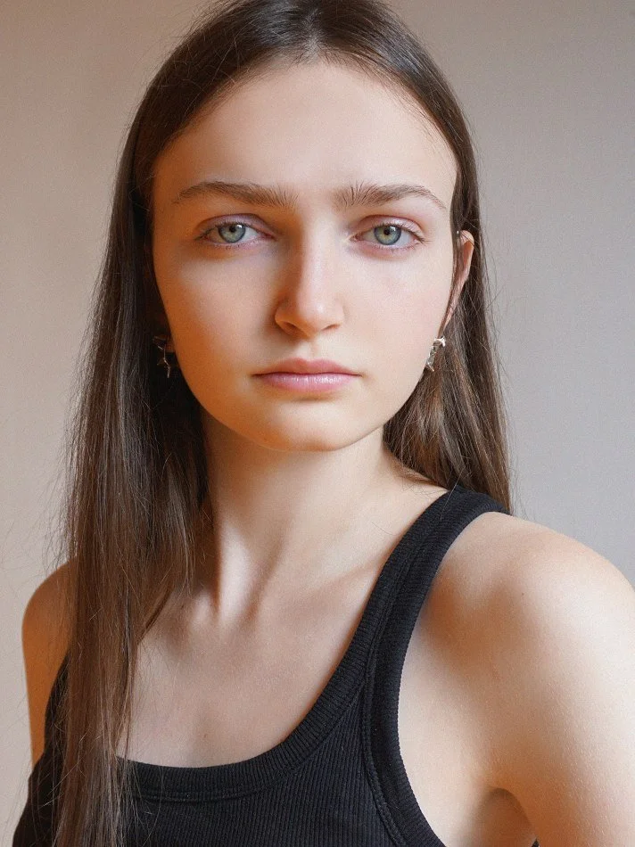 Close-up of Sadie, a young Montréal female model signed with MTL Models MGMT, with long brown hair, blue eyes, and light skin, wearing a black tank top and star-shaped earrings.