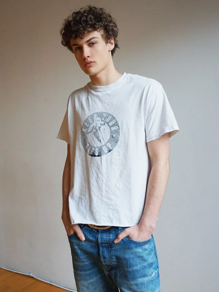 Albert, Montréal male model signed with MTL Models MGMT with curly hair modelling a white t-shirt and blue jeans, standing against a plain wall in a Montreal studio. Shot by photographer Melina Querel.