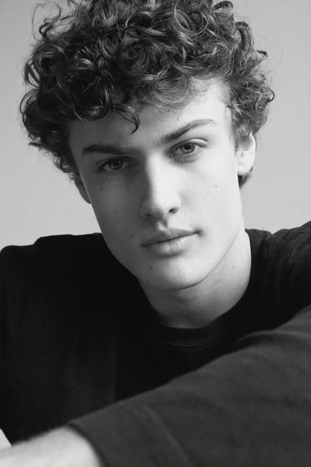 A young man with curly hair taking a selfie in black and white, wearing a black shirt.