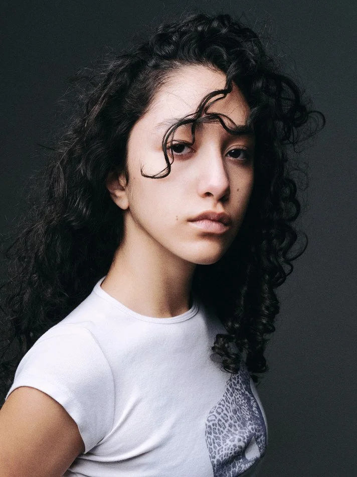 Oana, Montréal male model signed with MTL Models MGMT with curly black hair and fair skin, wearing a white t-shirt with a leopard print detail, modelling at the camera with a neutral expression.