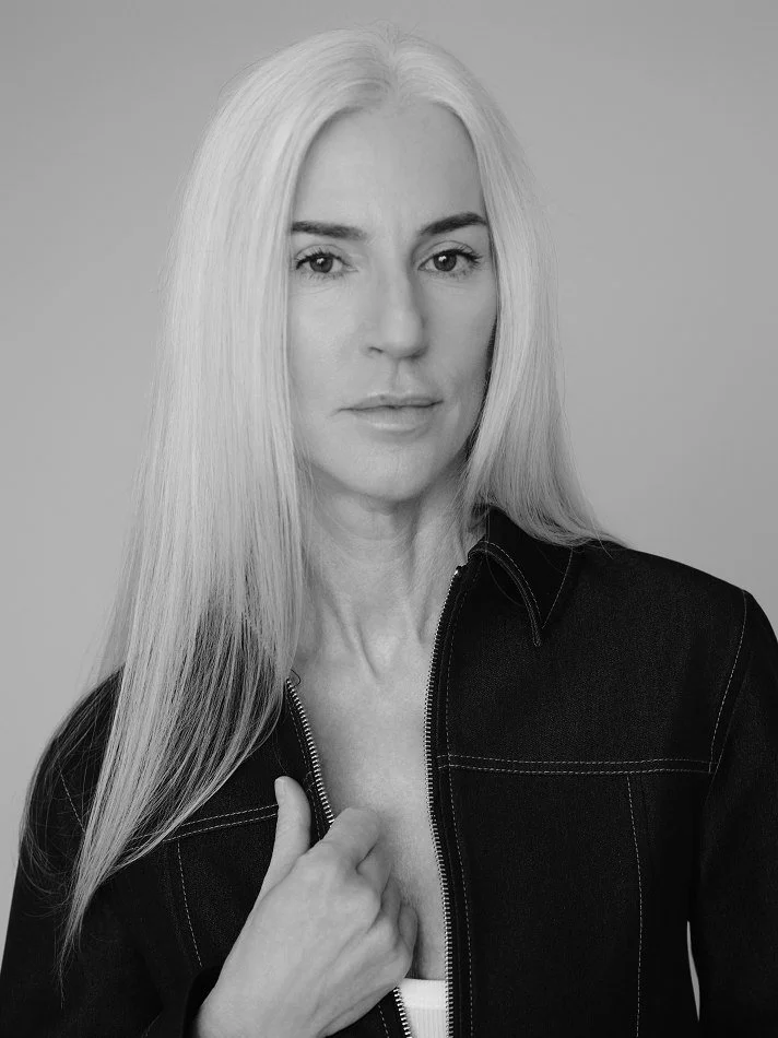 Black and white portrait of Carmen, Montréal female mature model signed with MTL Models MGMT with long, straight blonde hair. She is wearing a dark jacket and a light top underneath, with one hand holding the jacket near her chest.