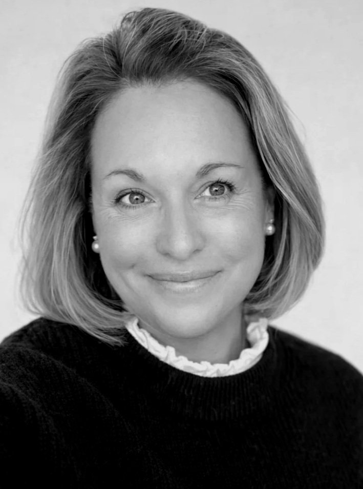 A black and white portrait of a woman with shoulder-length hair, smiling gently and wearing earrings and a dark sweater with a ruffled collar.