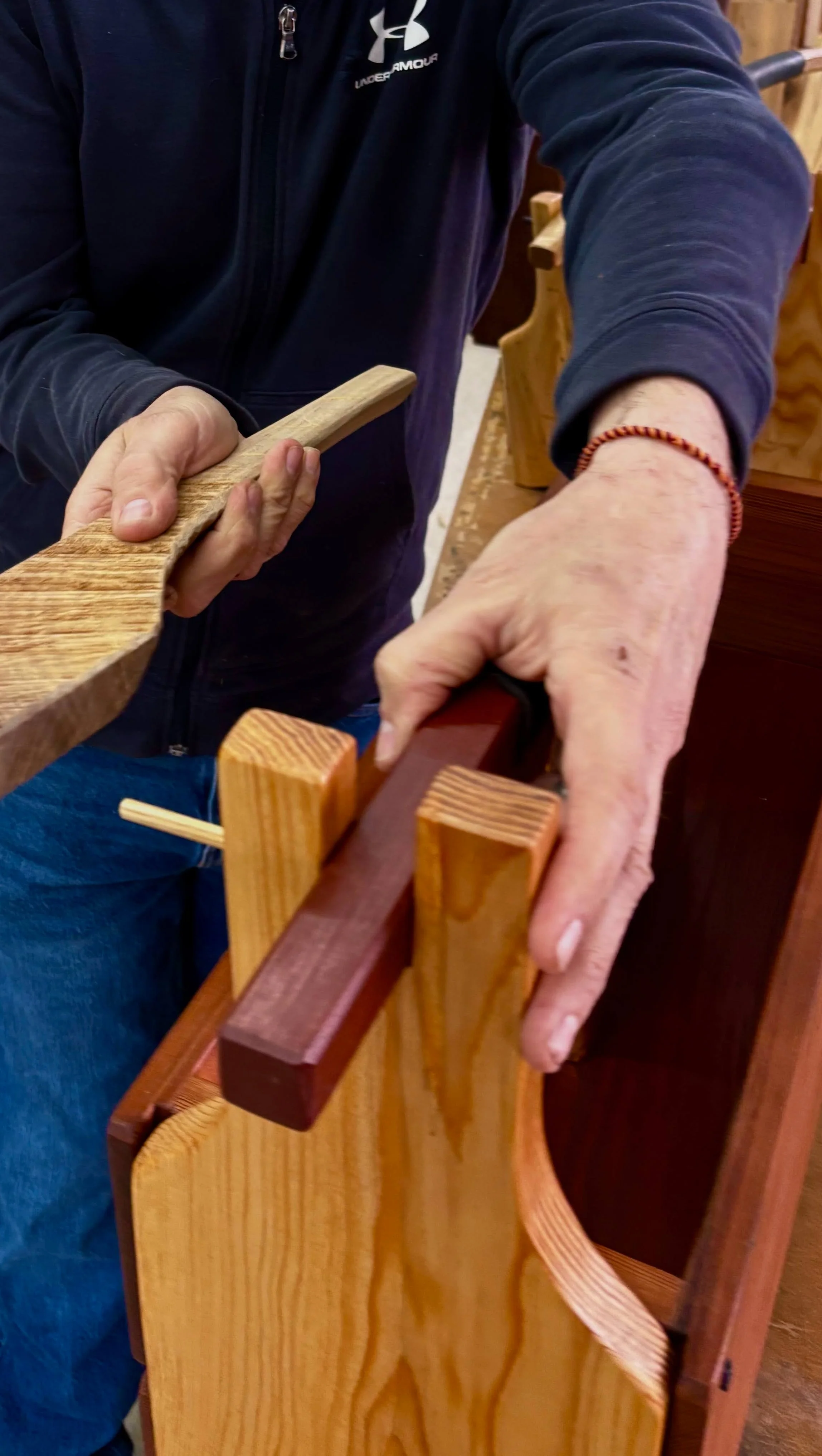 Craftsman Tim Pierce working on a woodworking project, holding a wooden piece and using a clamp on a wooden frame.