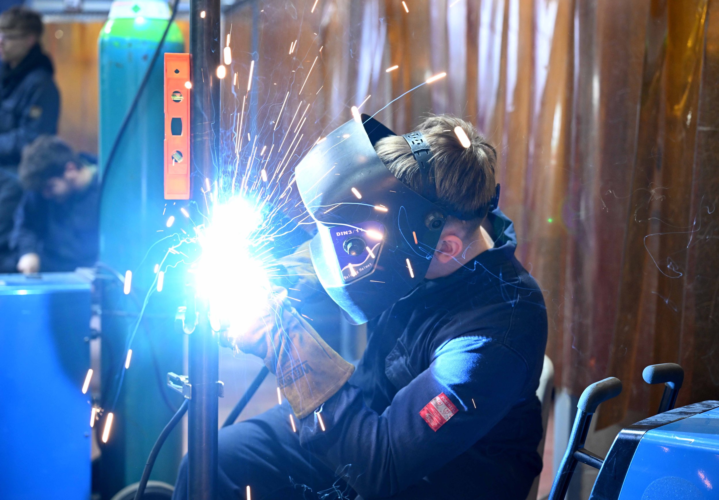 A person welding metal, wearing protective welding mask, sparks flying, in an industrial workshop.