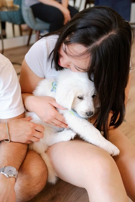 Woman with dark hair hugging a fluffy white puppy.