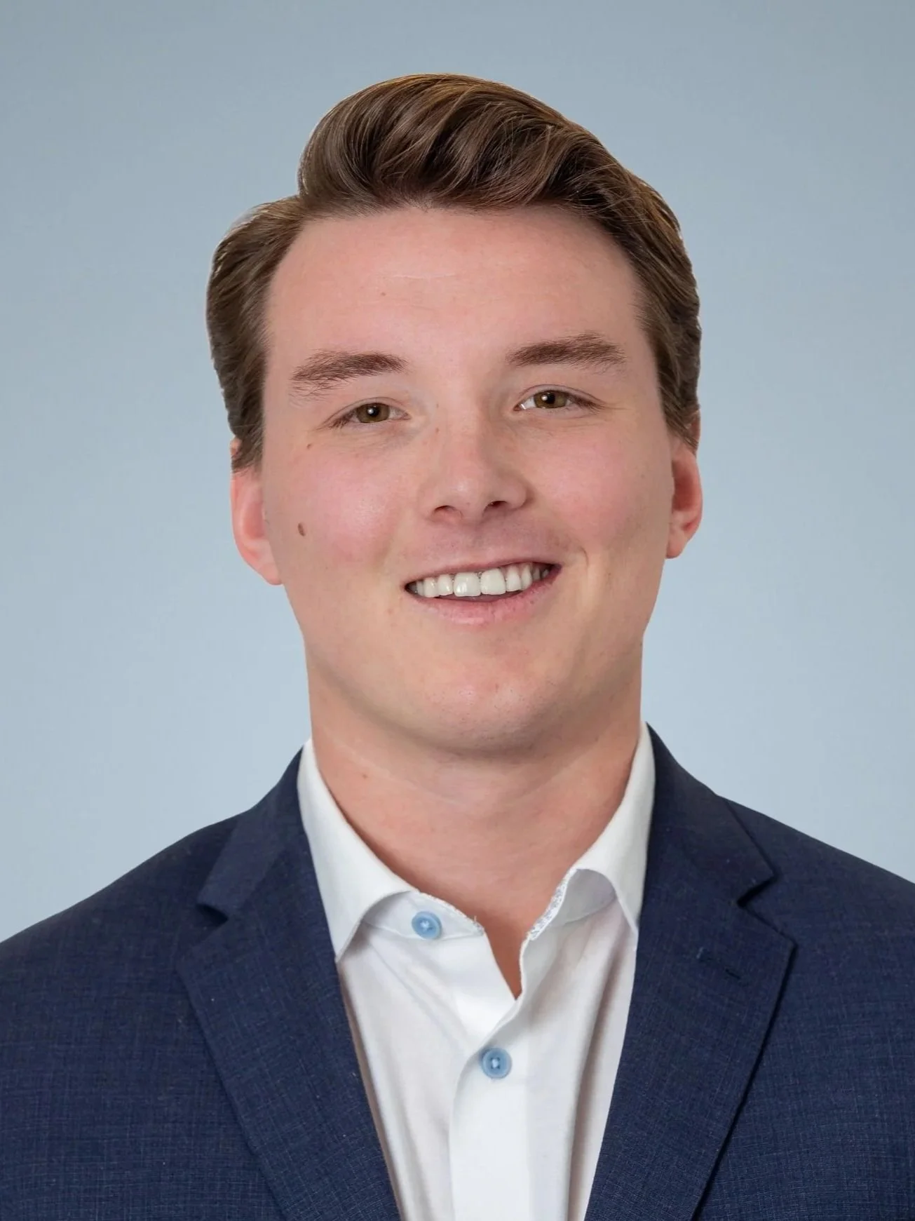 Headshot of a young man in a business suit smiling at the camera against a plain light background.