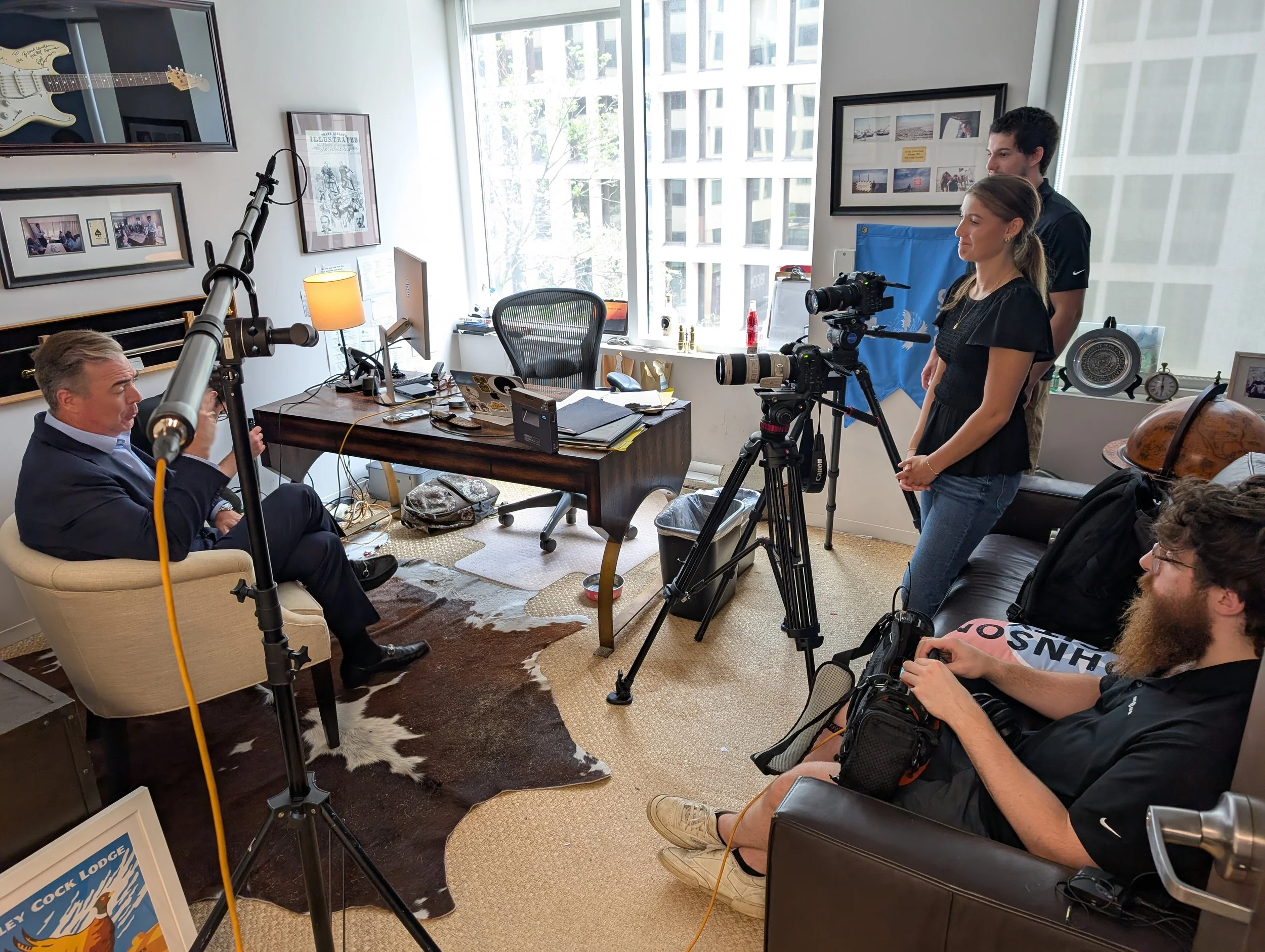 A seated man with a camera, alongside a cameraman setting up for a recording.