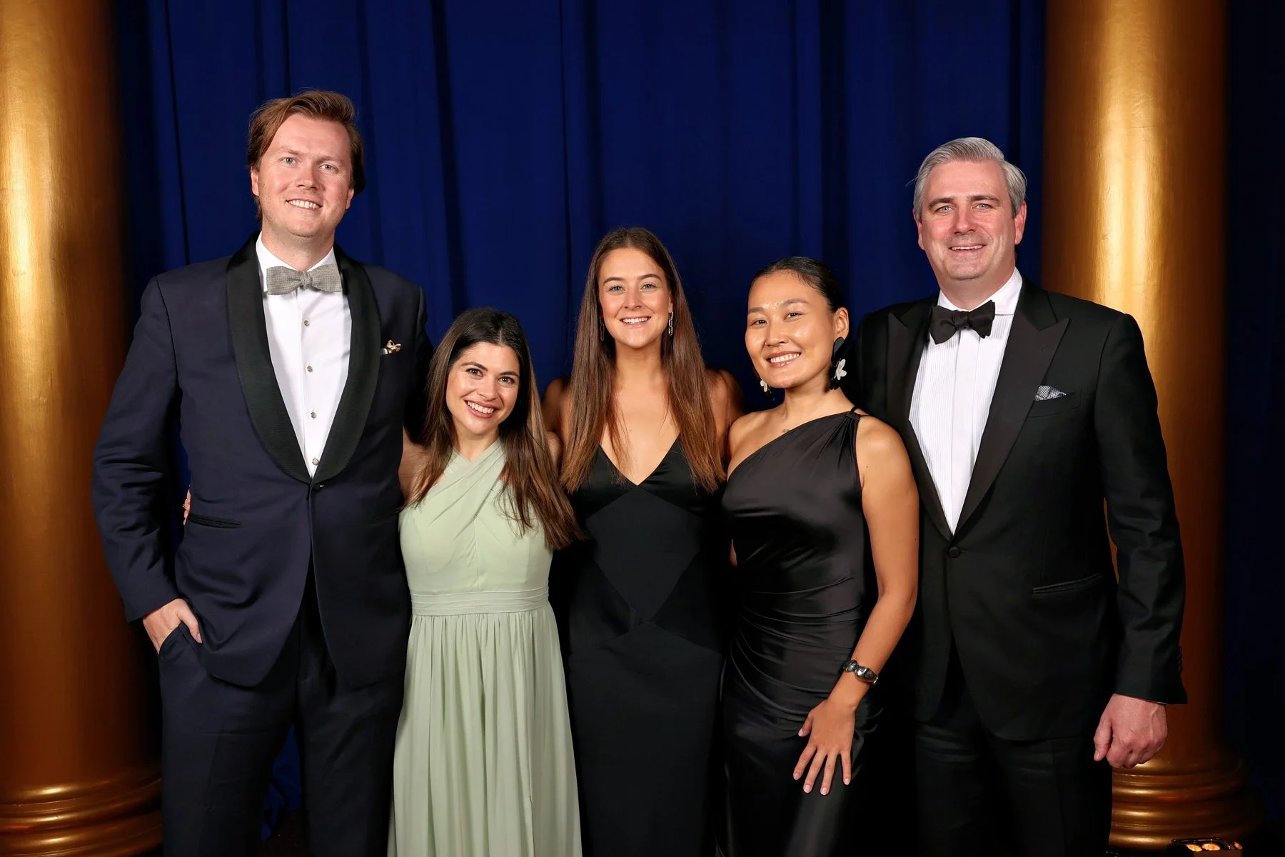 A group of people in formal attire smiling and posing together for a photo at a social event.