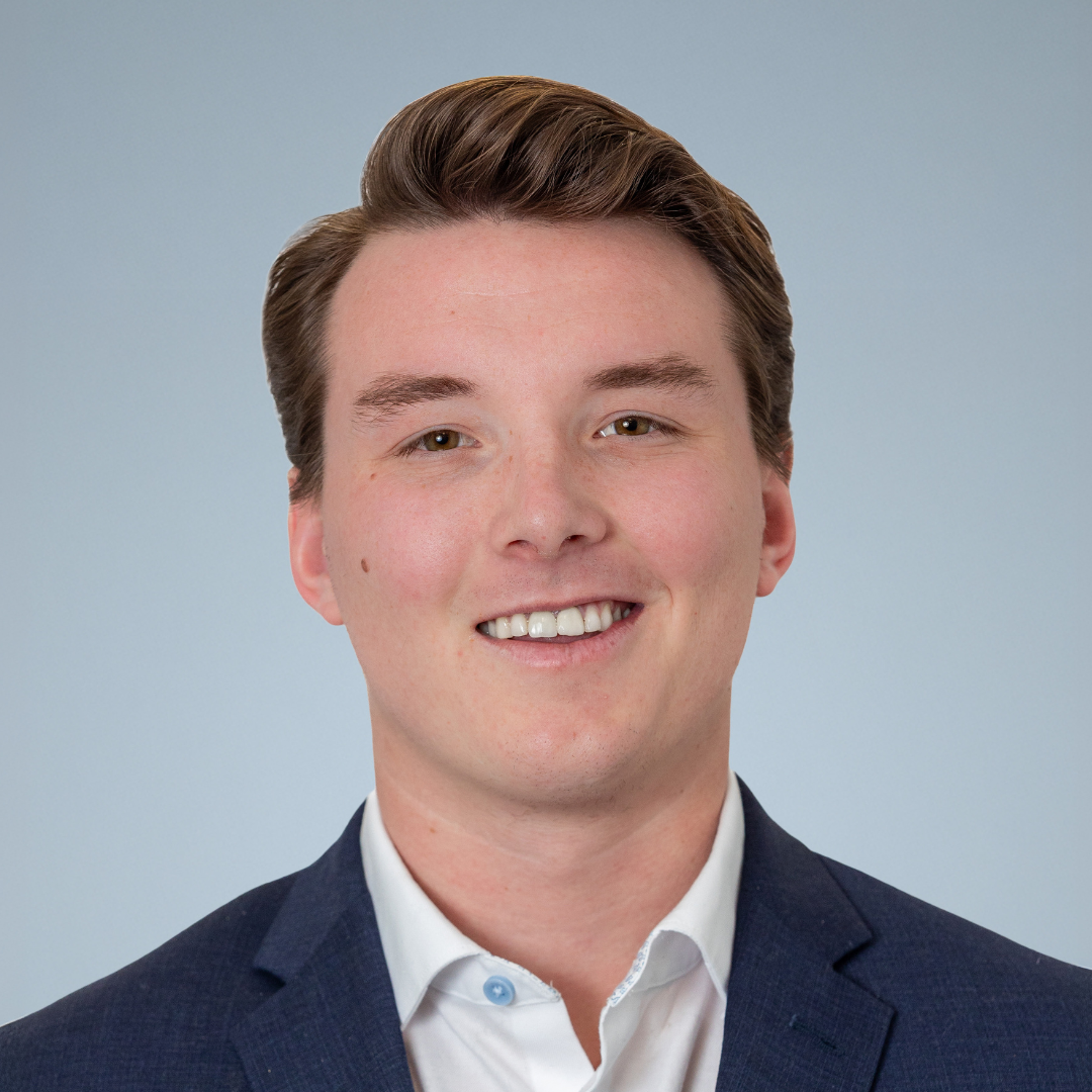 Young man in a business suit smiling against a light blue background.