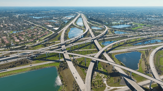 Aerial view of multiple interconnected highways and bridges over lakes and cityscape in the background.