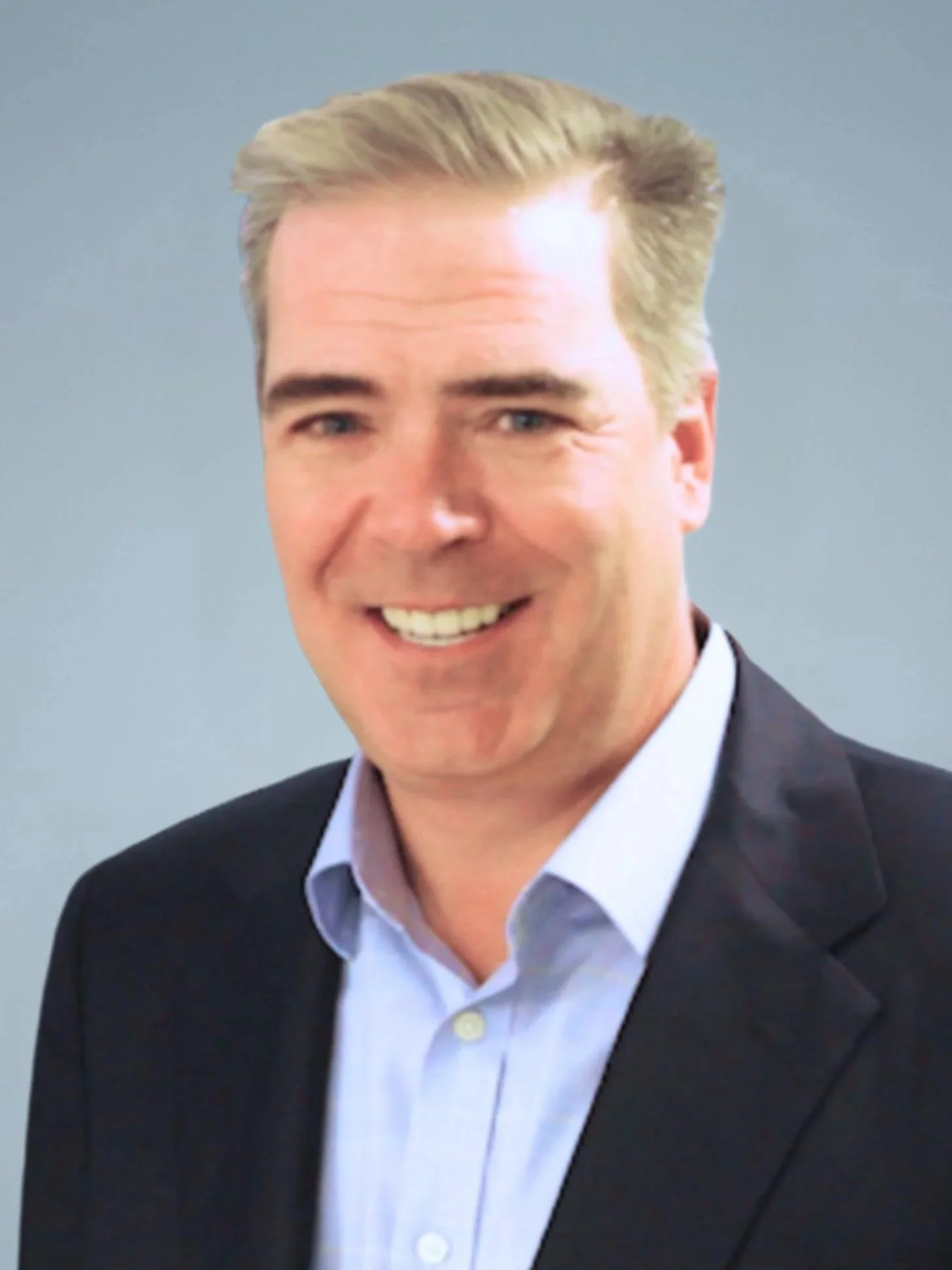 A smiling man with blonde hair wearing a dark suit jacket and light-colored dress shirt, posing against a neutral background.