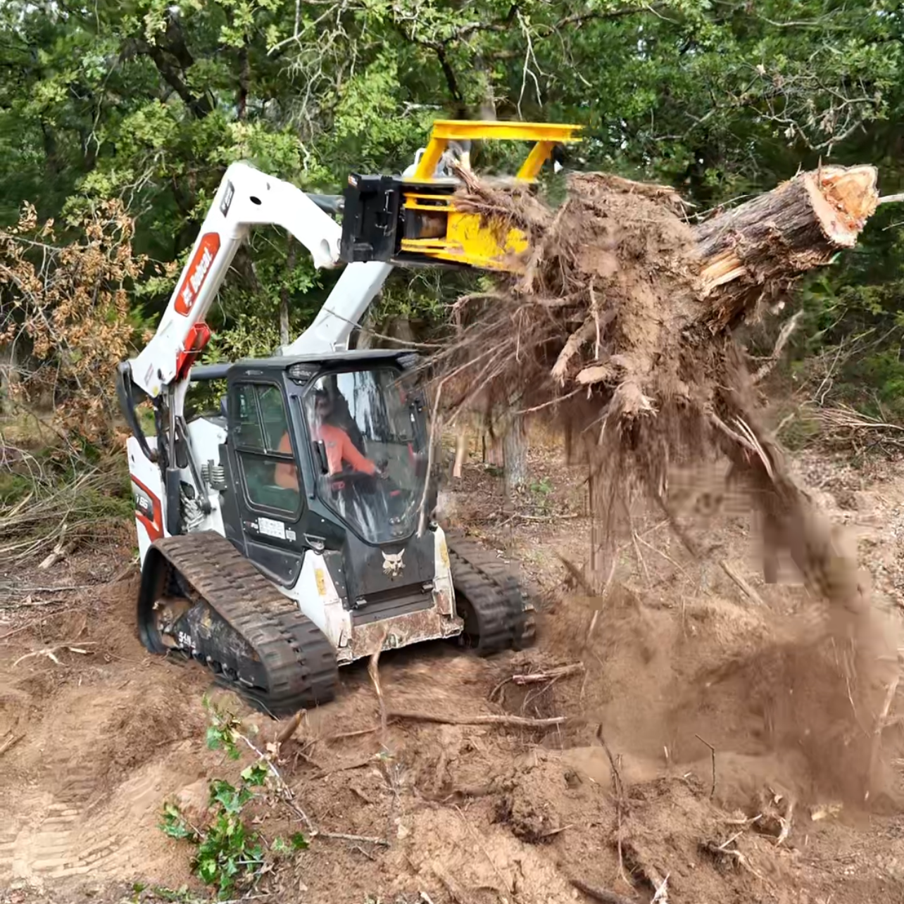 A person operating a mini excavator bulldozing a large uprooted tree in a wooded area.