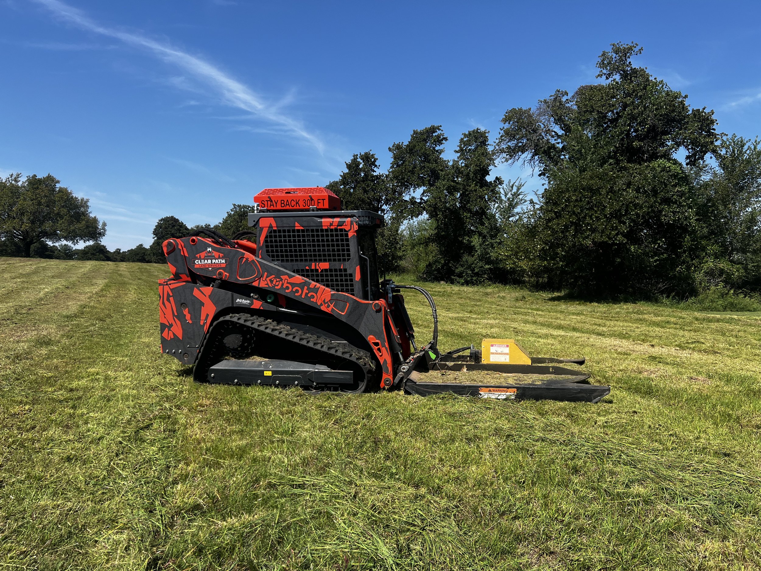 A Kubota zero-turn mower on a grassy field under a blue sky with scattered clouds.