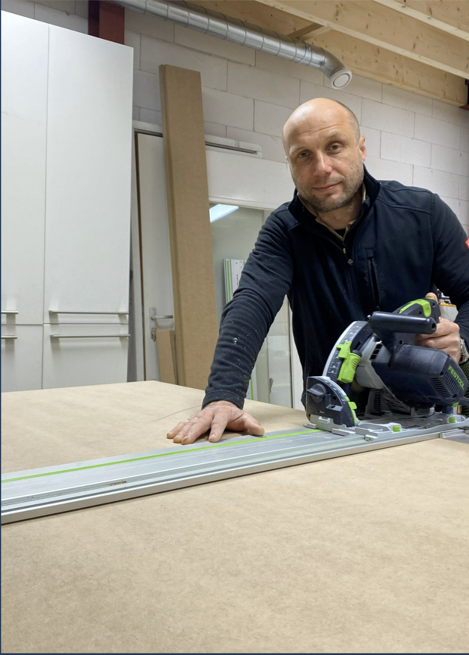Man die een cirkelzaag op een werkbank bedient in een houtwerkplaats.