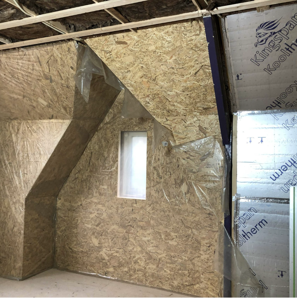 Binnenkant van een gebouw onder constructie met gipsplaten en isolatiemateriaal.