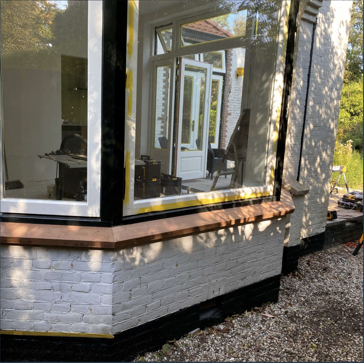 Een renovatie van een u-vormige uitbouw met grote ramen en een Franse deur, met zichtbaar bouwmateriaal en gereedschap.
