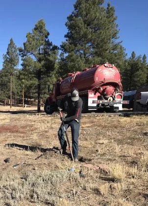 Man digging in the dirt with a red Durango septic tank behind him. 