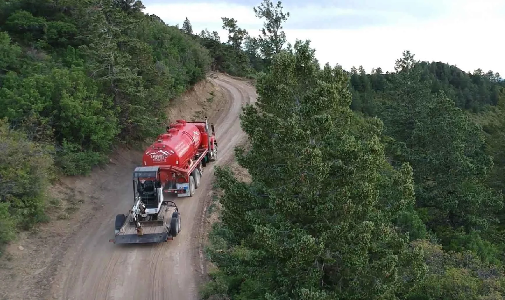 a Durango Septic truck driving up a dirt road in La Plata county pulling a Bobcat Excavator